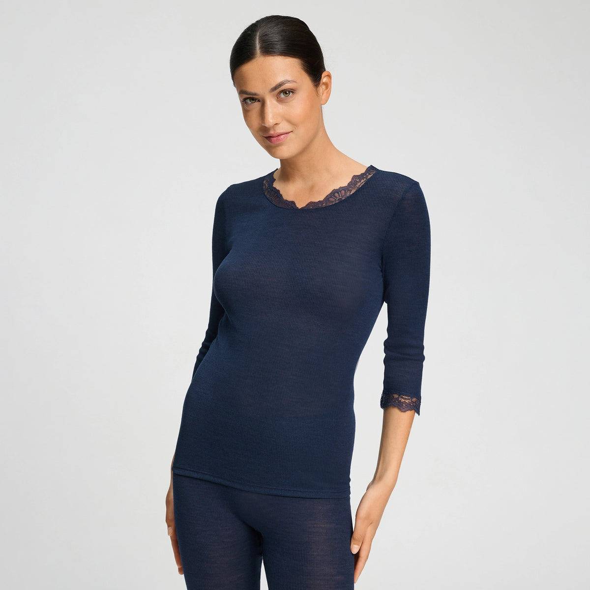 A woman modelling a dark navy blue long-sleeve top with a sheer lace crew neck and matching lace cuffs, paired with matching navy leggings, against a light grey studio background.