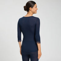 A back view of woman modelling a dark navy blue long-sleeve top with a sheer lace crew neck and matching lace cuffs, paired with matching navy leggings, against a light grey studio background.