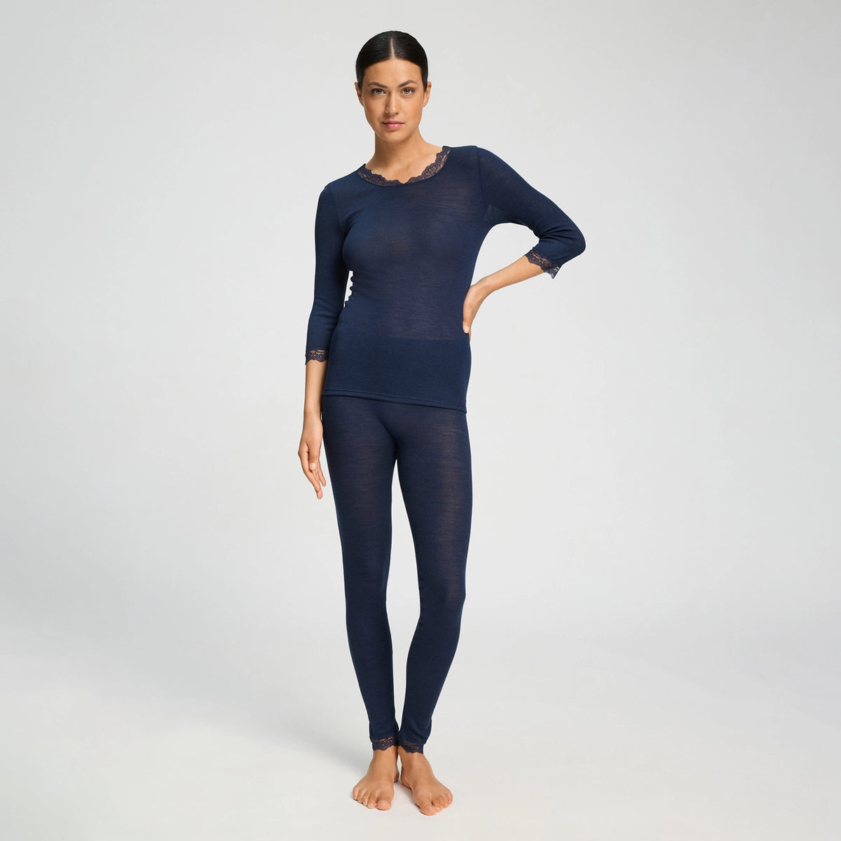 A woman modeling a matching navy blue two-piece knit loungewear set, featuring a long-sleeve top with lace trim at the neckline and cuffs, paired with matching full-length leggings, against a light gray studio background.