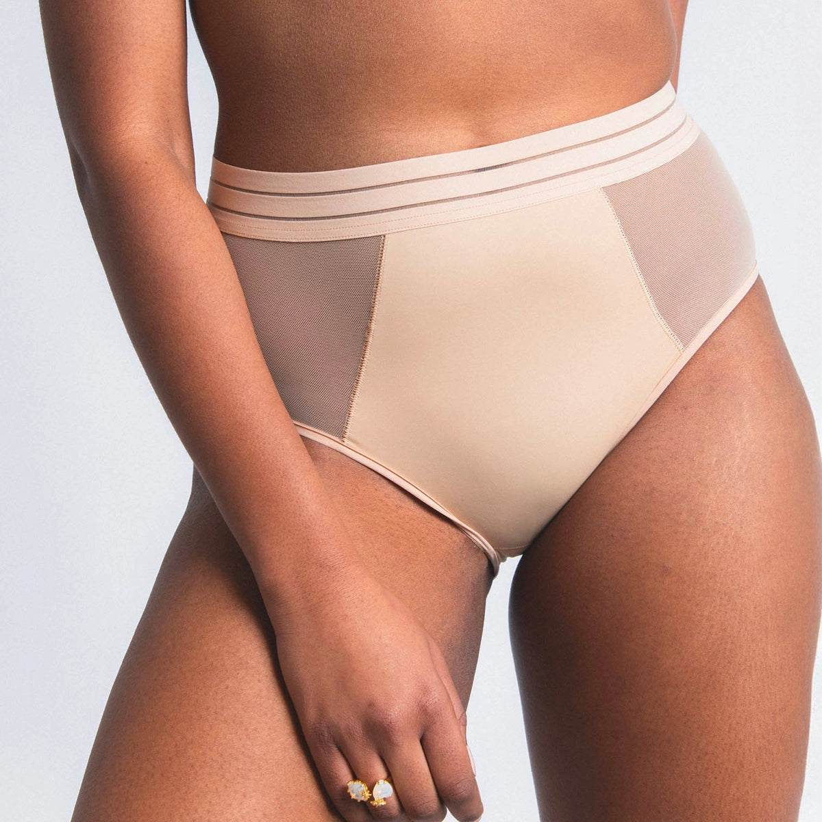 beige underwear with mesh panels worn by a person on a light gray background