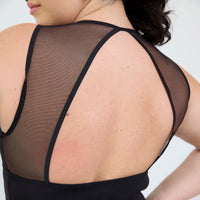 Close-up back view of a woman wearing a black sheer mesh sports bra or tank top with black trim straps against a light gray studio background.