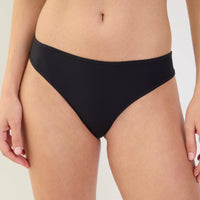 A close-up of a model wearing a solid black bikini bottom against a clean, light off-white background.