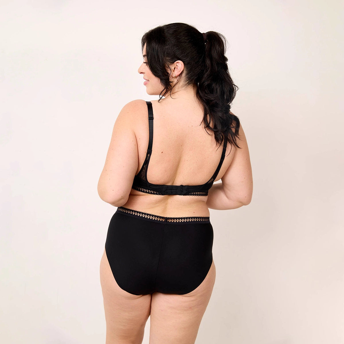 woman wearing a black swimsuit with lace details on a beige background