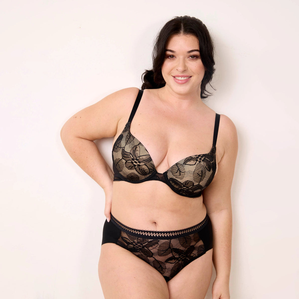 woman wearing a black lace bra and panties set against a plain background
