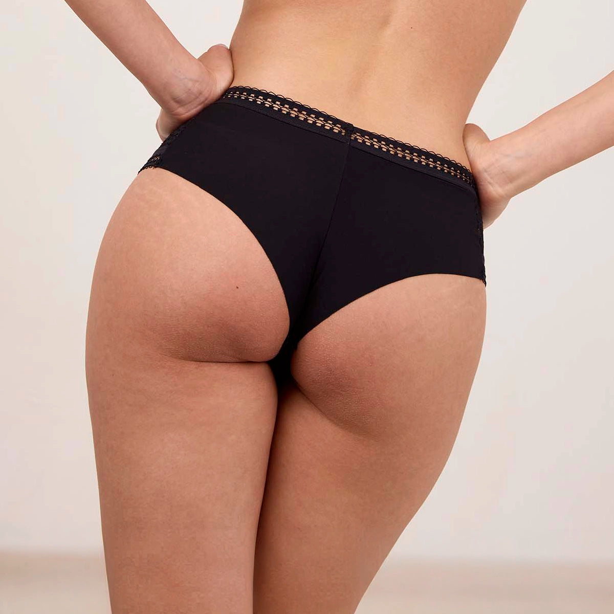person wearing black underwear with lace trim on a neutral background