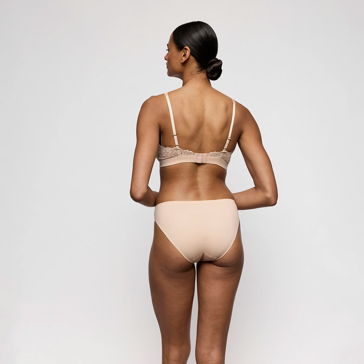 woman wearing a beige bra and panties set against a plain background