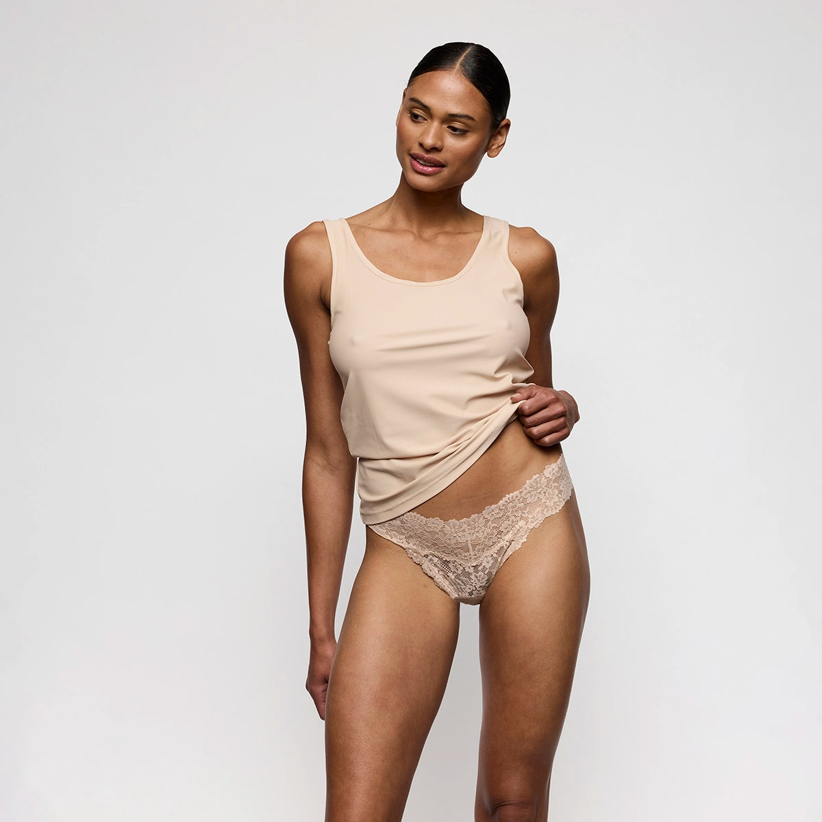 woman wearing a beige tank top and lace underwear against a plain background