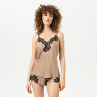 a women wearing satin camisole in golden beige colour with thin straps and black v neck trim and matching shorts on a plain background