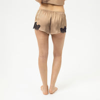 a crop of a women's body in back wearing satin shorts with black lace trim at the hem, shown on a plain grey background