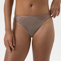 A close-up of a model wearing a taupe brown lace and solid mesh thong underwear against a light gray background.