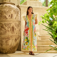 woman in a colourful dress standing next to a large decorative urn with plants around.