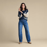 A woman modeling a navy and cream knit sweater with blue wide-leg jeans and tan shoes, standing against a solid beige studio background.