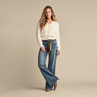 A model wearing jumper and a pair of high-waisted blue denim jeans with a patterned scarf tie belt in beige, green, and black, set against a plain  background.