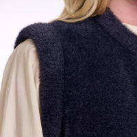 Close-up of a person wearing a dark navy fuzzy sleeveless vest over a cream-colored blouse, with blonde hair visible at the top.