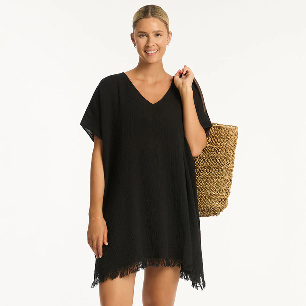 woman wearing a black cover-up dress holding a straw bag on a white background