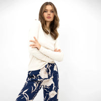 Close-up of a model wearing a cream long sleeve top paired with navy blue trousers featuring a white floral print, against a white studio background.