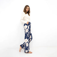 Model wearing a cream long sleeve top and navy blue wide-leg trousers with a white floral print, shown from the side against a white studio background.