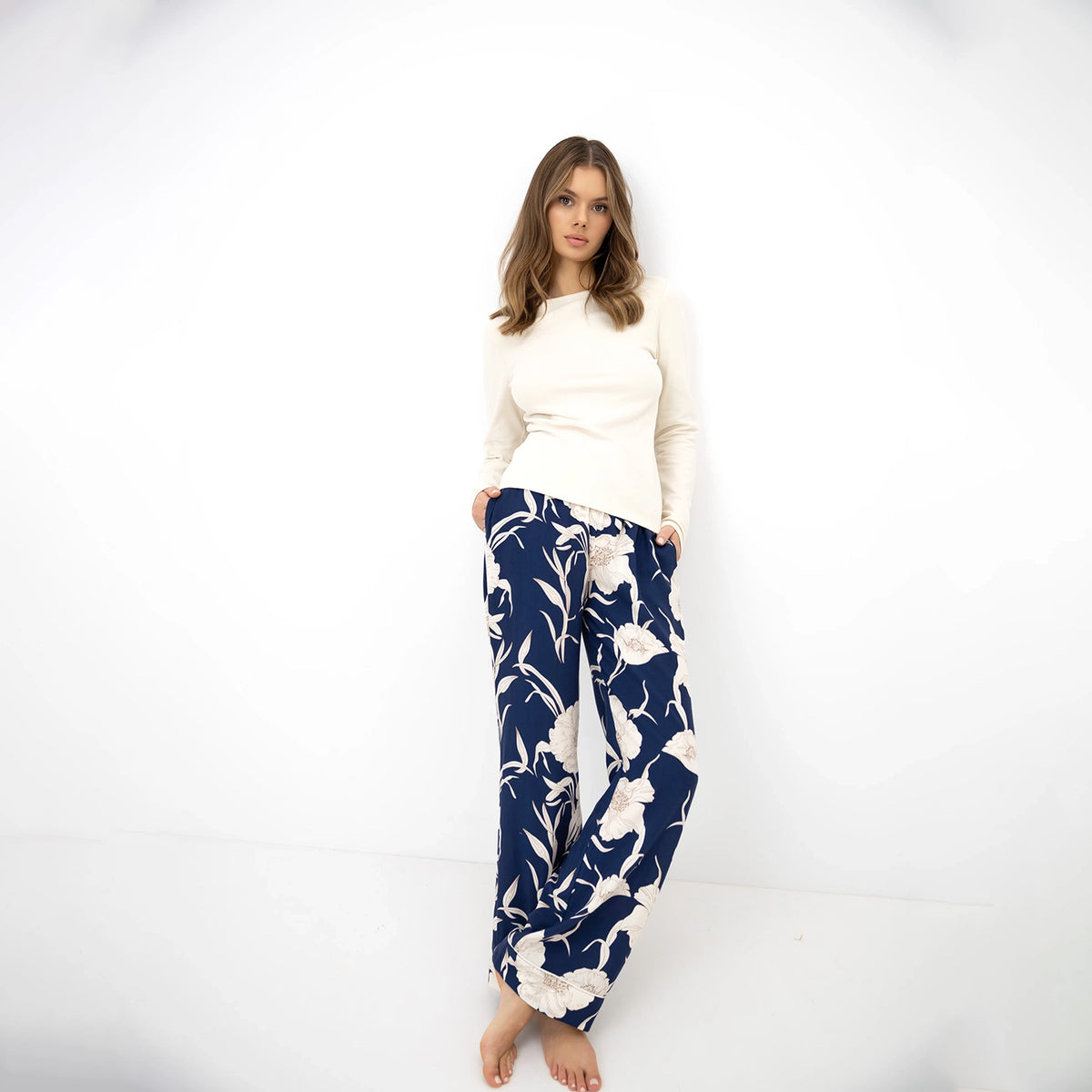 Model wearing a cream long sleeve top with navy blue wide-leg trousers featuring a white floral print, styled barefoot against a white studio background.