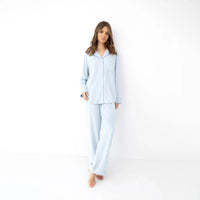 Model wearing a light blue long-sleeve pyjama set with a button-up collared top, chest pocket and matching wide-leg trousers, against a white studio background.