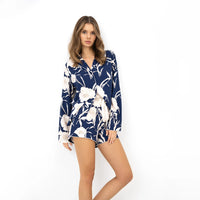 A woman modeling a navy blue long-sleeve pyjama set with a white floral print, set against a plain white studio background.