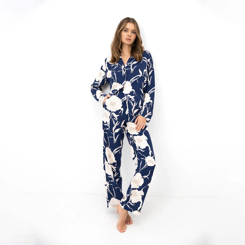 A woman modelling a matching long-sleeve pyjama set with a navy blue and cream floral print, photographed against a seamless white studio background.