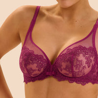 A close-up of a woman wearing a magenta lace and mesh underwire bra against a light beige background.