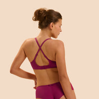 A woman shown from the back wearing a matching magenta-purple sports bra and high-waisted brief set against a solid beige background.