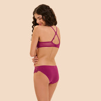 A woman modeling a magenta mesh bralette and matching high-waisted briefs, shown from the back against a solid beige background.