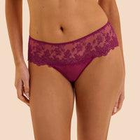 A model wearing a pair of magenta lace panties against a solid beige background.