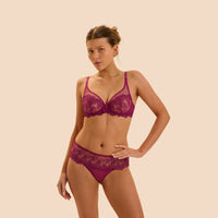 A woman modeling a matching magenta lace bra and panty set against a solid beige background.