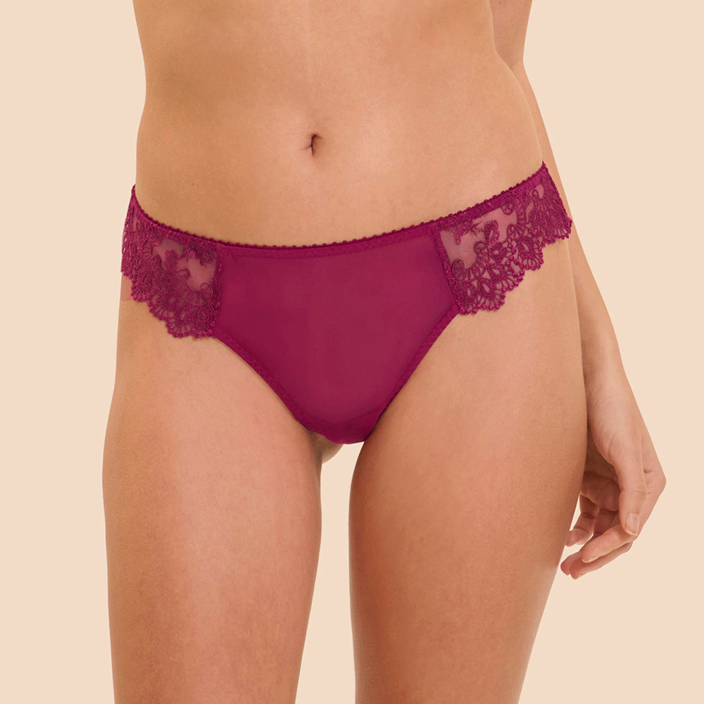 A close-up of a model wearing magenta lace and mesh panties against a solid beige background.