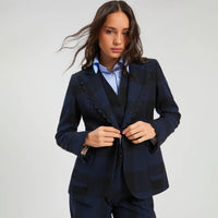A woman modeling a dark navy blue plaid blazer with distinctive scalloped edges, worn over a matching vest and a light blue collared shirt, against a plain light gray studio background.