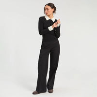 Model wearing a fitted black ribbed long-sleeve top with a contrasting cream pointed collar and cuffs, paired with black wide-leg trousers and patterned flat shoes.