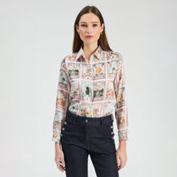 A woman modeling a long-sleeve button-up shirt with a colorful patchwork print of vintage playing cards, paired with dark blue jeans, against a plain light gray background.