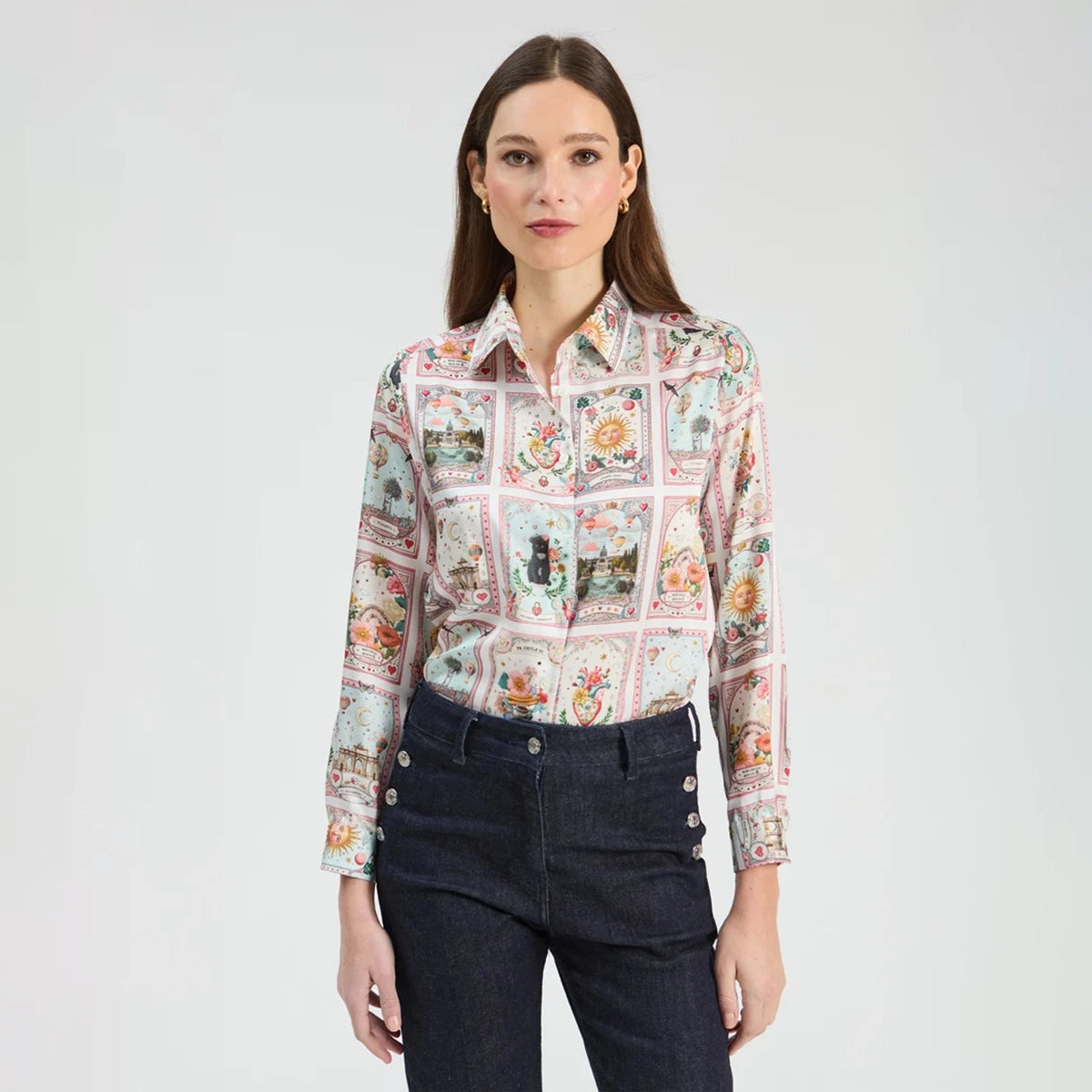 A woman modeling a long-sleeve button-up shirt with a colorful patchwork print of vintage playing cards, paired with dark blue jeans, against a plain light gray background.