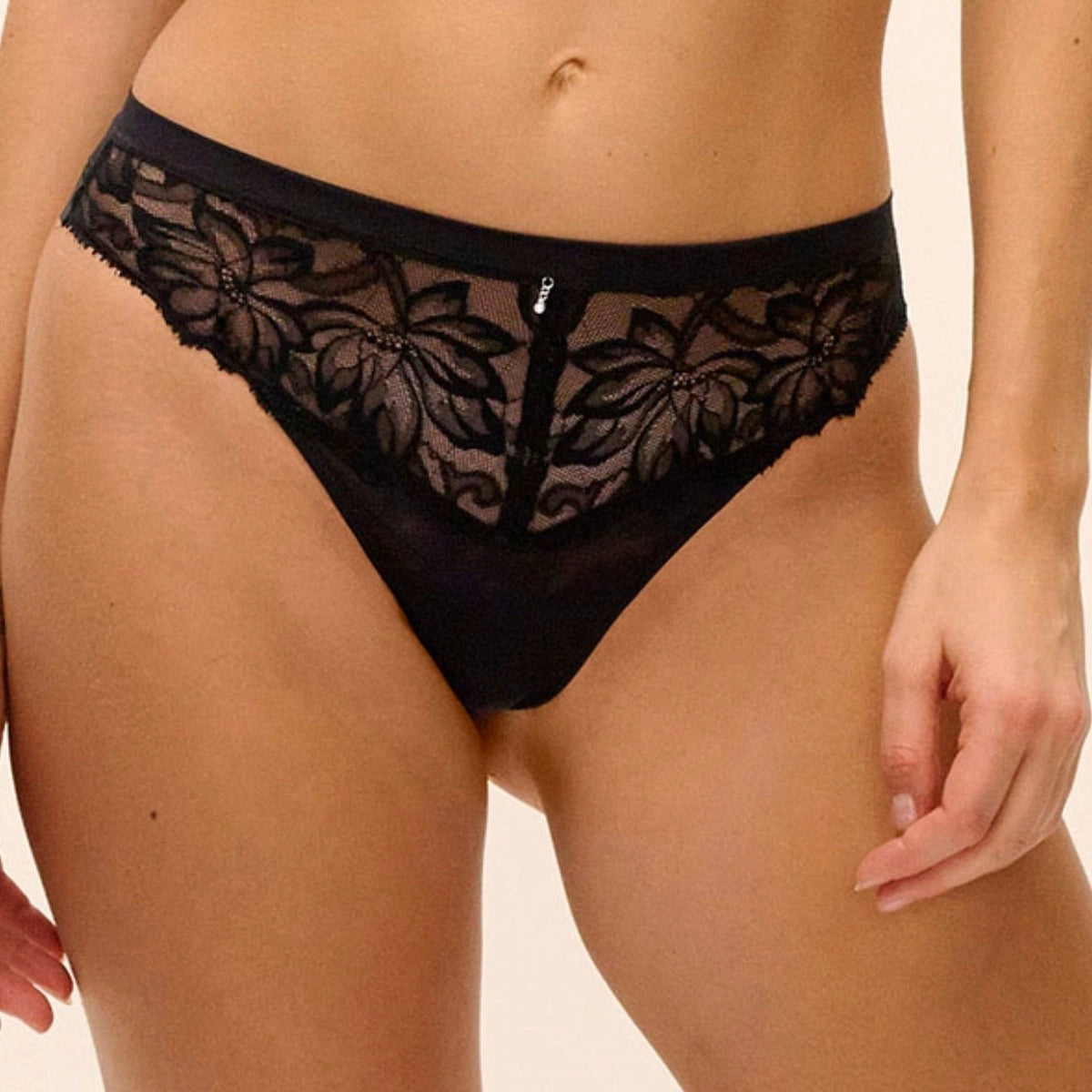 Black lace thong underwear with a floral lace pattern, shown on a model against a light beige background.