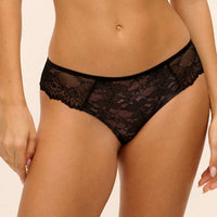 Black lace panties worn by a model, shown from the waist to upper thighs against a plain light beige studio background.