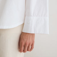 Close-up of a person wearing a white long-sleeve button-up shirt with a wide cuff and a light beige textured skirt or pants, with the hand resting near the fabric.