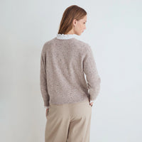A woman shown from the back wearing a light taupe speckled knit sweater with a white ruffled collar, paired with beige trousers, against a plain light gray background.