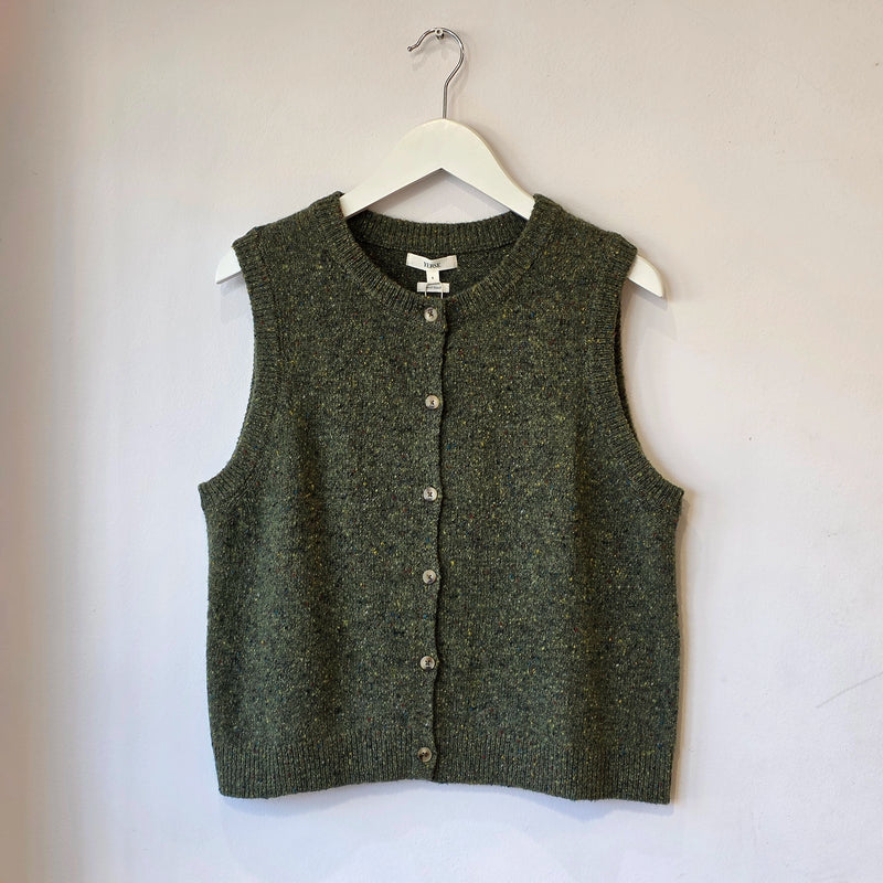 An olive green knit button-front vest hanging on a white hanger against a plain off-white wall.