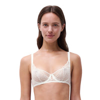 A woman modeling a white lace underwire bra against a solid white background.