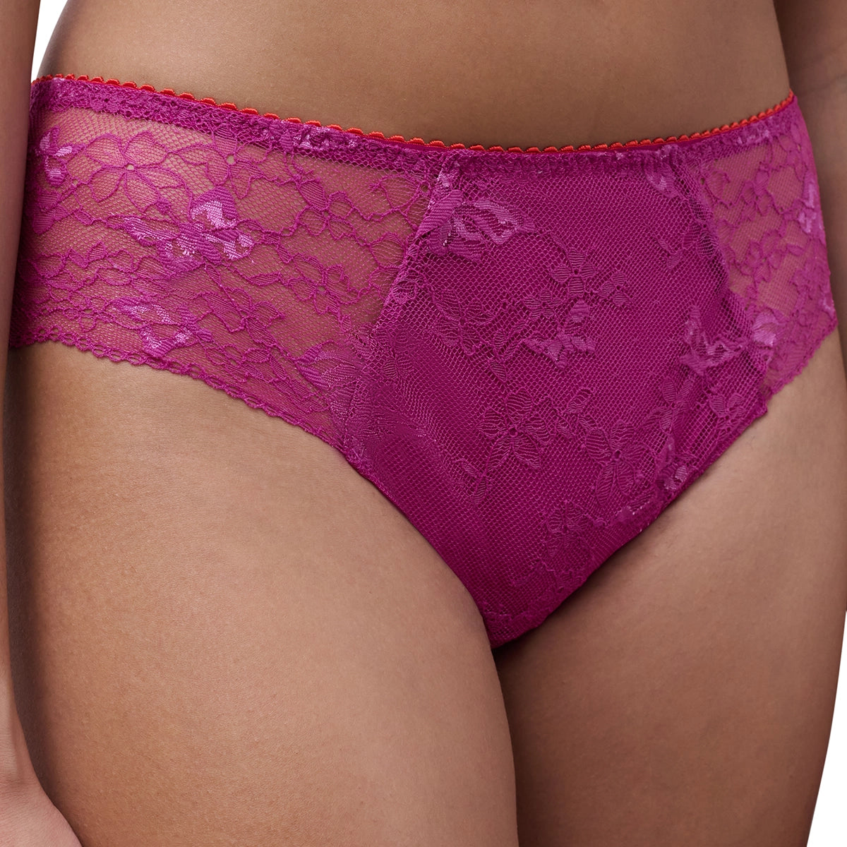 A close-up of a model wearing a magenta lace panties with sheer mesh panels and a red stitched waistband.