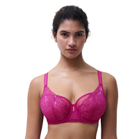 A woman modeling a bright pink lace underwire bra against a plain white background.
