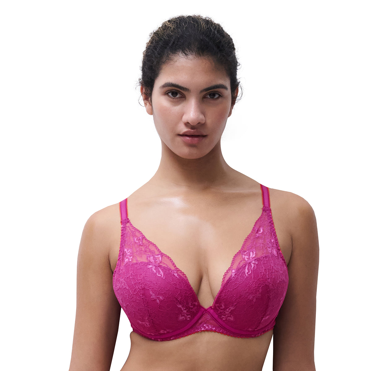 A woman modeling a bright pink lace underwire bra against a plain white background.
