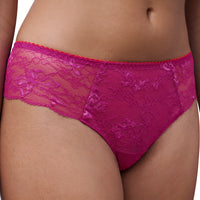A close-up of a model wearing bright magenta lace panties with a sheer mesh panel and floral lace pattern.