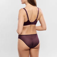 A woman shown from the back wearing a matching deep plum lingerie set, featuring a bralette with lace-up back straps and high-waisted briefs, against a plain light gray studio background.