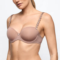 Woman wearing a beige bra with decorative straps on a light gray background