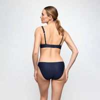 A woman shown from the back wearing a dark navy textured bikini set against a light gray studio background.
