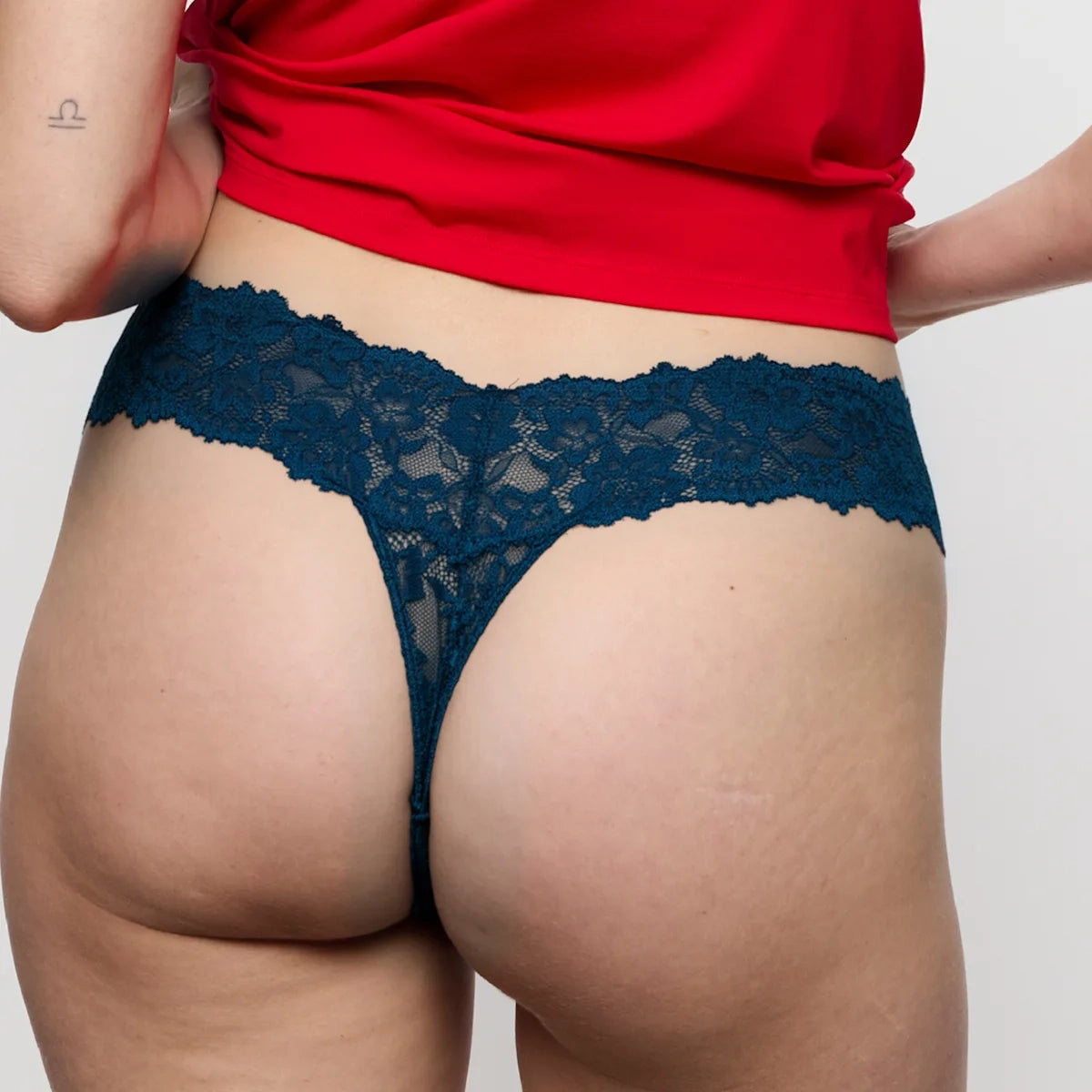Person wearing a red top and blue lace underwear on a plain background
