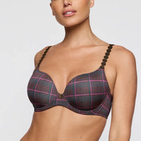 A close-up of a woman wearing a plaid underwire bra with dark brown beaded straps against a light gray background.